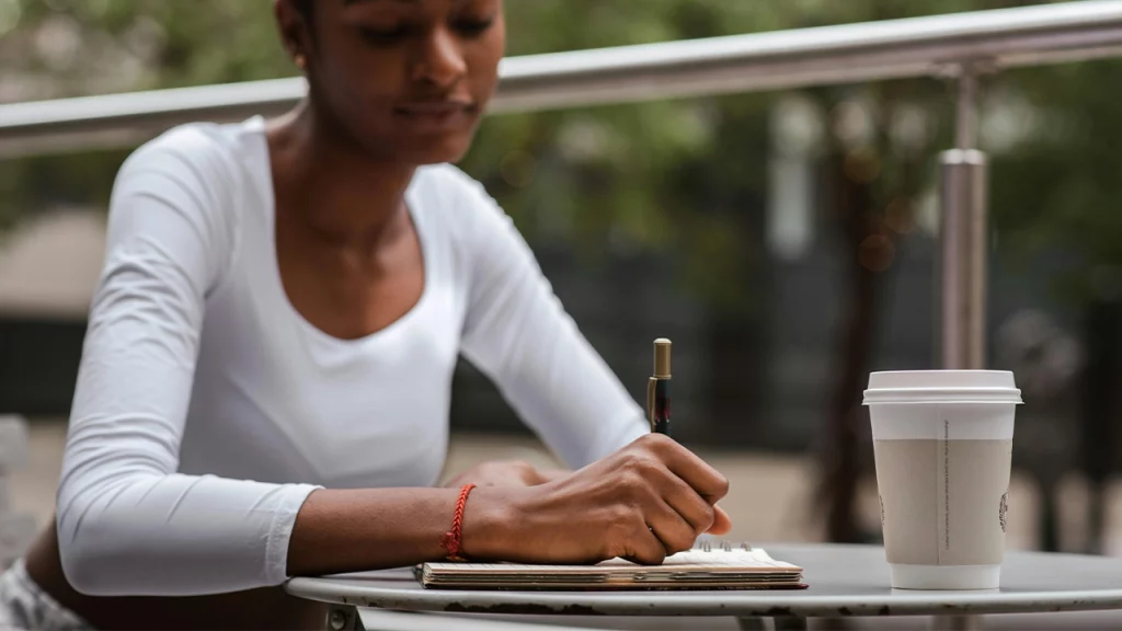 Redactor médico tomando café y escribiendo en una terraza.
